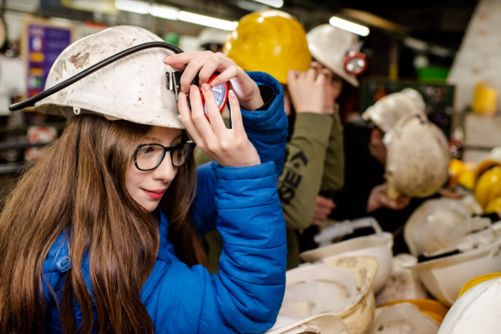 Young girl trying on a white hard hat before an Underground Tour.