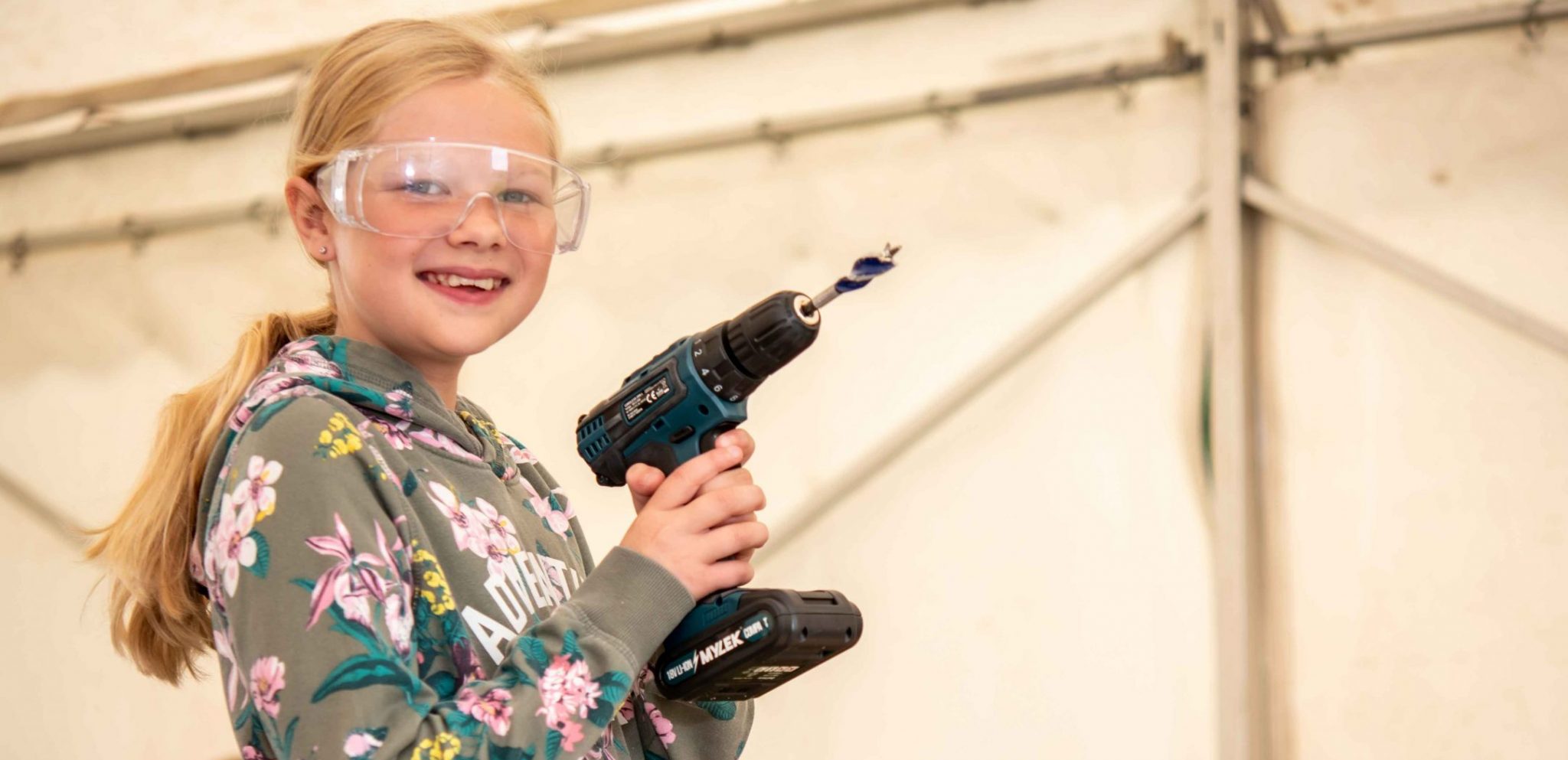 A girl holding a drill and wearing clear safety goggles