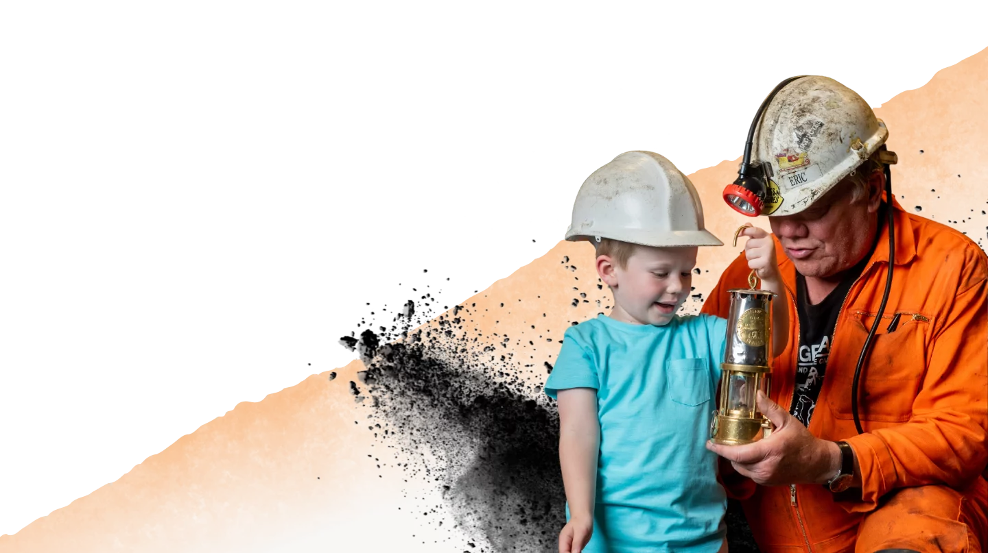 About Us Child and a mine guide looking at a Miner's Lamp up close