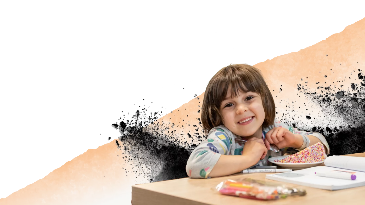 Cafe A child smiling with a large slice of colourful cake and a colouring book in front of her