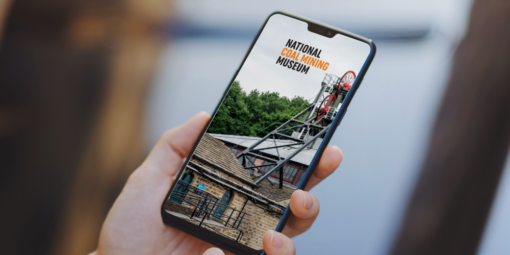 Smartphone being held by a hand showing the Bloomberg Digital Guide homescreen