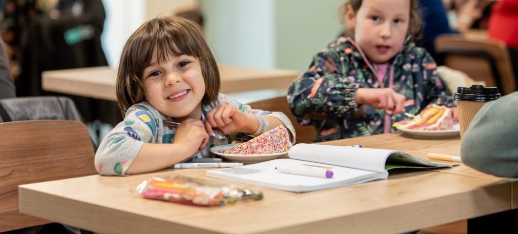 Two young children sitting at a table in the cafe - drawing on a pad on the table