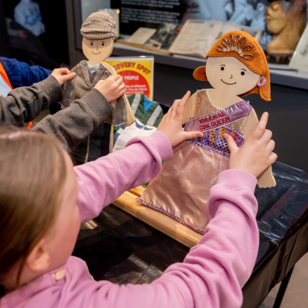 Two children dress wooden dolls in coal queen and miner outfits